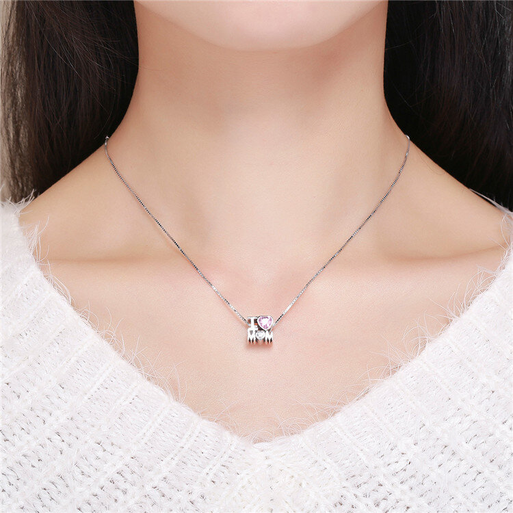 Na szyi osoby znajduje się srebrny naszyjnik z zawieszką w kształcie napisu \'I ♥ MOM\'. Serce w napisie jest ozdobione różowym kamieniem.