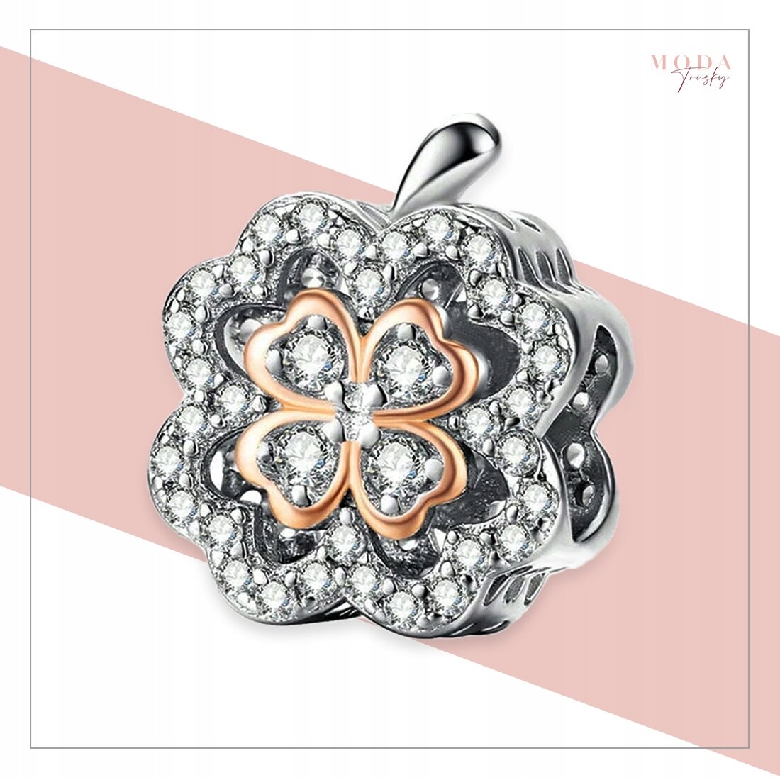 Na obrazie widoczny jest charms w kształcie koniczyny, ozdobiony błyszczącymi kamieniami i elementami w kolorze złotym. W prawym górnym rogu znajduje się napis \'MODA Jewelry\'.