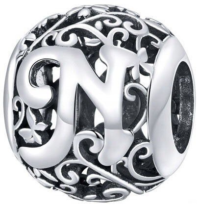Srebrna zawieszka charms z literą \'N\' otoczona ozdobnym, ażurowym wzorem. Wykonana z metalu o błyszczącej powierzchni.