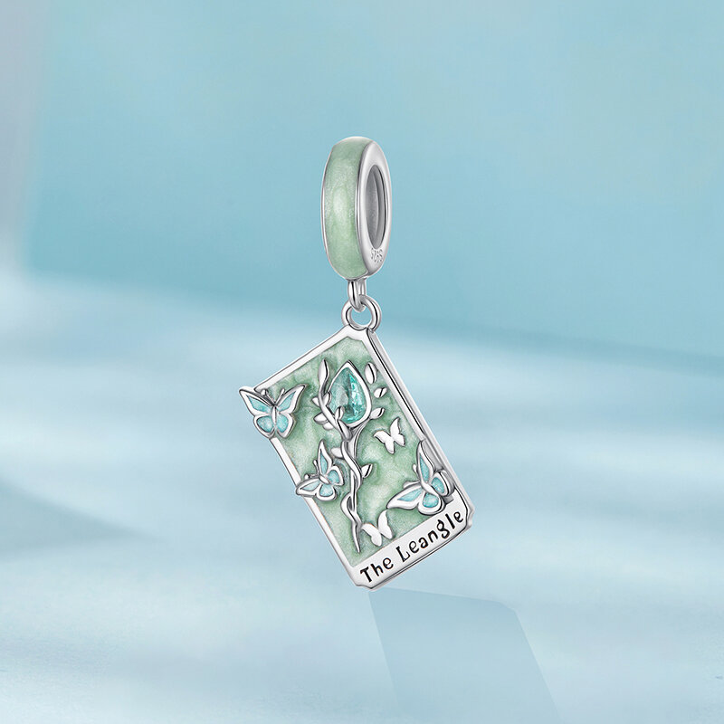 Srebrna zawieszka charms z motywem karty tarota, ozdobiona motylami i kwiatem na zielonym tle. Na dole widoczny jest napis \'The Leangle\'.