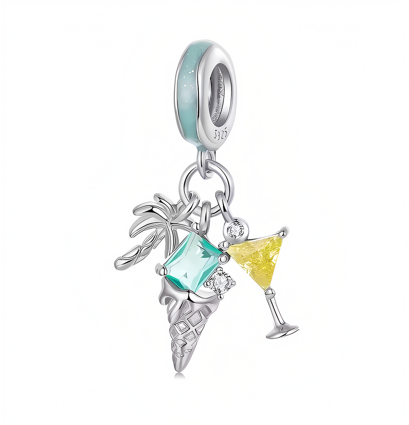 Srebrna zawieszka charms z trzema elementami: palmą, lodem w rożku i kieliszkiem z żółtym napojem. Widoczny jest także niebieski kamień oraz oznaczenie \'925\' na obręczy.
