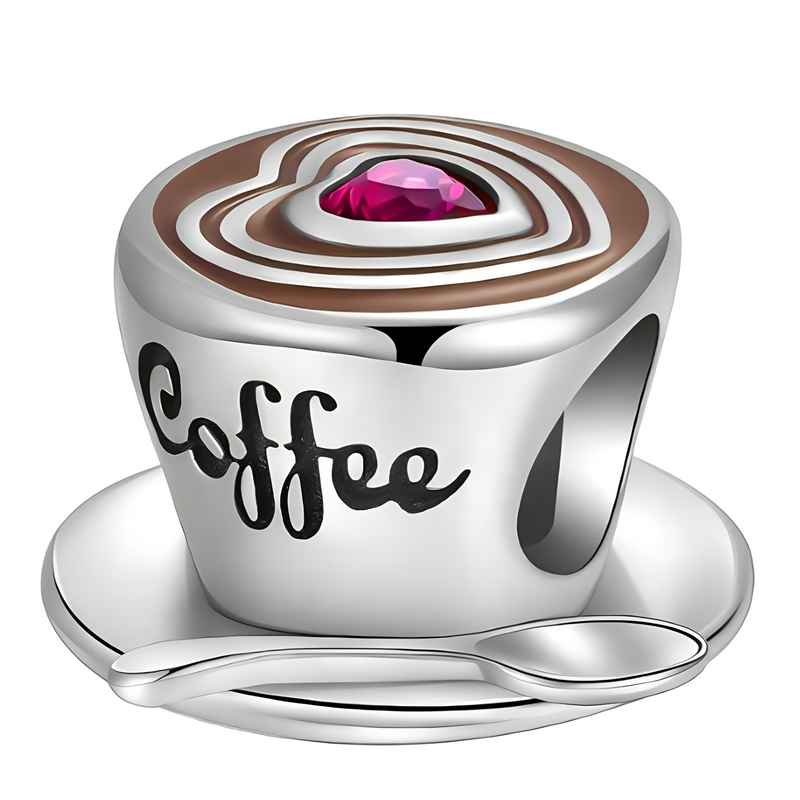 Srebrna zawieszka w kształcie filiżanki z napisem \'Coffee\', ozdobiona różowym kamieniem na wierzchu. Filiżanka stoi na spodku z łyżeczką.