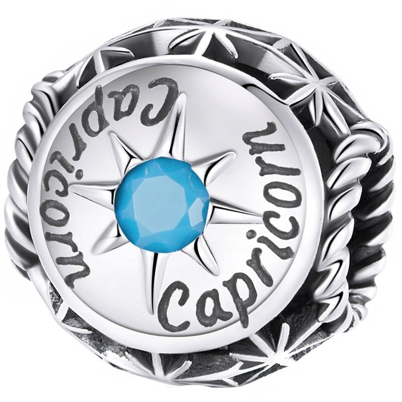 Srebrny charms z napisem \'Capricorn\' i niebieskim kamieniem w centrum, otoczony wzorem przypominającym gwiazdy.
