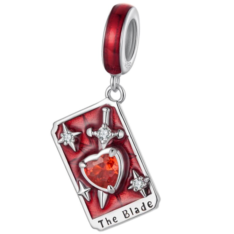 Zawieszka charms w kształcie karty tarota z czerwonym sercem i mieczem na tle, ozdobiona srebrnymi elementami. Na dole widnieje napis \'The Blade\'.