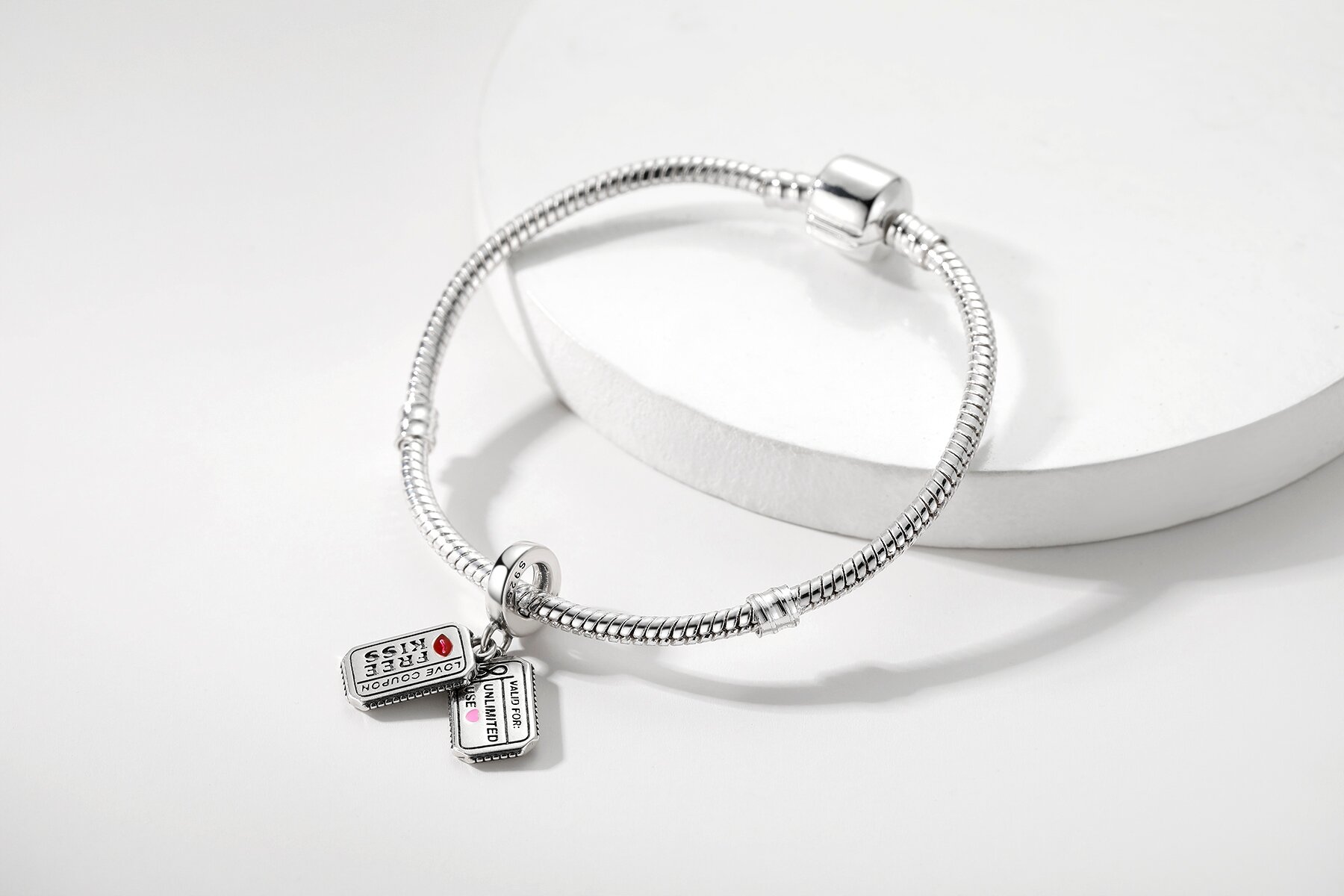 Srebrna bransoletka z zawieszkami w kształcie kuponów, na których widnieje tekst \'SAVE $25\' i \'LIMITED EDITION\'. Bransoletka leży na białym tle.