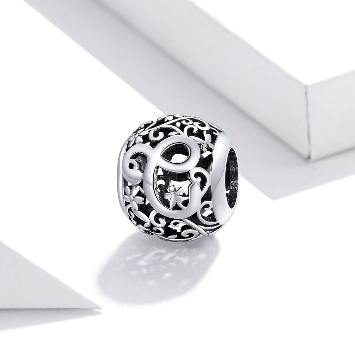 Srebrna zawieszka charms z literą \'C\' ozdobiona delikatnymi wzorami i motywem kwiatowym. Produkt jest umieszczony na białym tle.