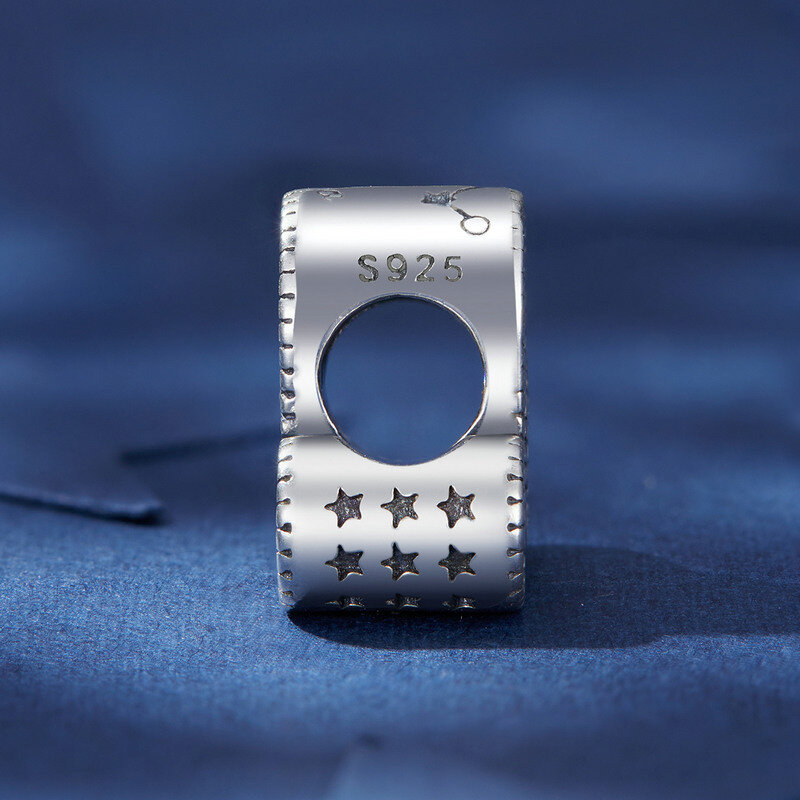 Srebrna zawieszka charms z oznaczeniem \'S925\' i wzorem gwiazdek na niebieskim tle. Widoczny jest także symbol przypominający konstelację.