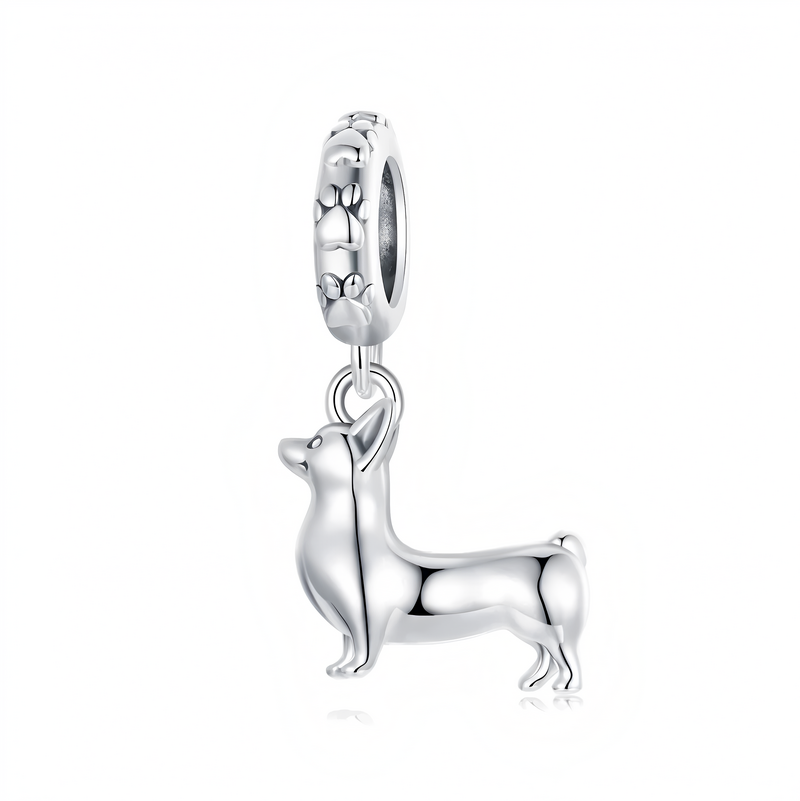Srebrna zawieszka charms w kształcie psa rasy corgi, wykonana z połyskującego metalu. Okrągły element mocujący ozdobiony jest wzorem łapek.