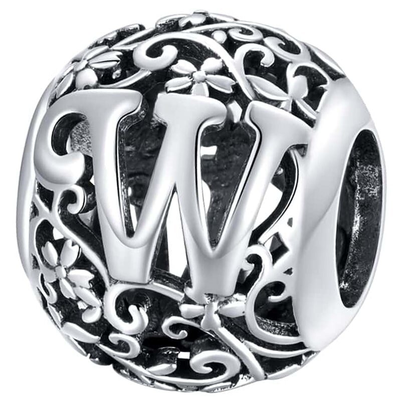 Srebrna zawieszka charms z literą \'W\' otoczona ozdobnym wzorem z kwiatami i liśćmi. Wykonana z metalu o błyszczącej powierzchni.