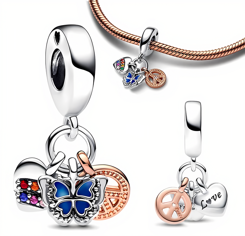 Na obrazie widoczne są trzy zawieszki charms, w tym motyl z niebieskimi skrzydłami, symbol pacyfki w kolorze różowego złota oraz serce z napisem \'Love\'. Zawieszki są przymocowane do srebrnej bransoletki.