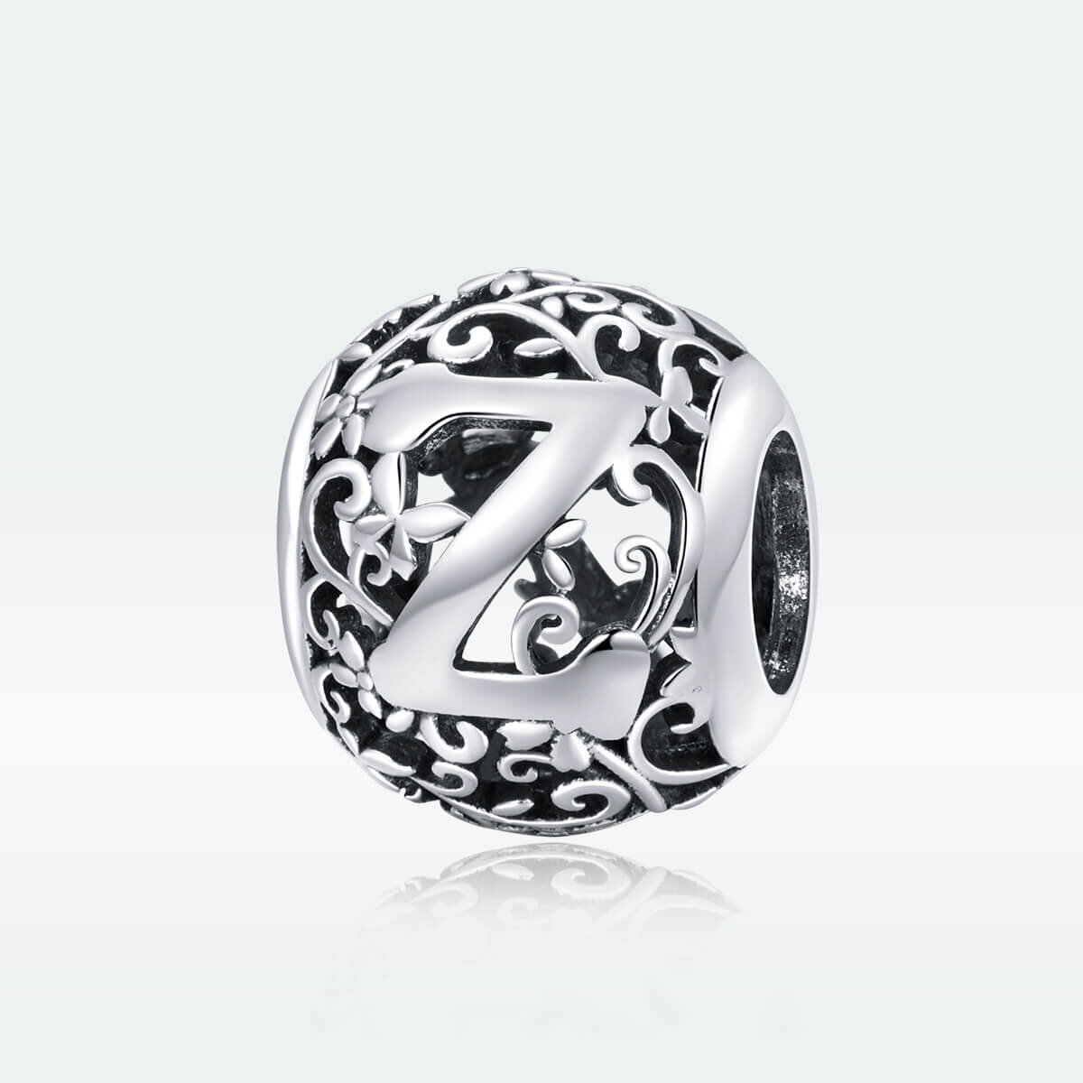 Srebrna zawieszka charms z literą \'Z\' otoczona ozdobnym, ażurowym wzorem z motywem roślinnym. Wykonana z metalu o błyszczącej powierzchni.