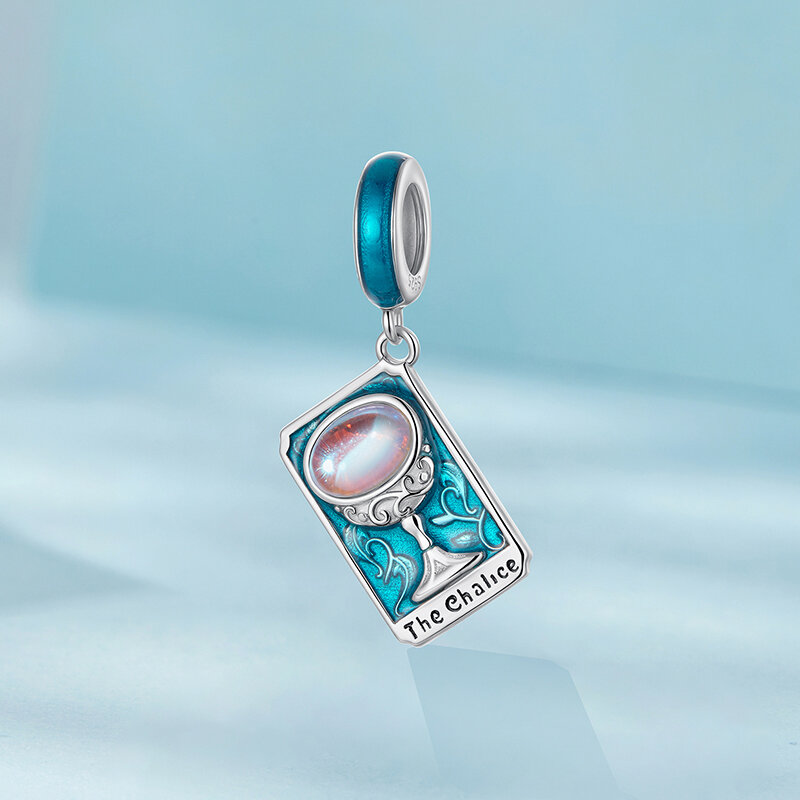 Zawieszka charms w kształcie karty tarota z napisem \'The Chalice\', ozdobiona niebieskim kamieniem i srebrnym kielichem. Tło jest w odcieniach niebieskiego.