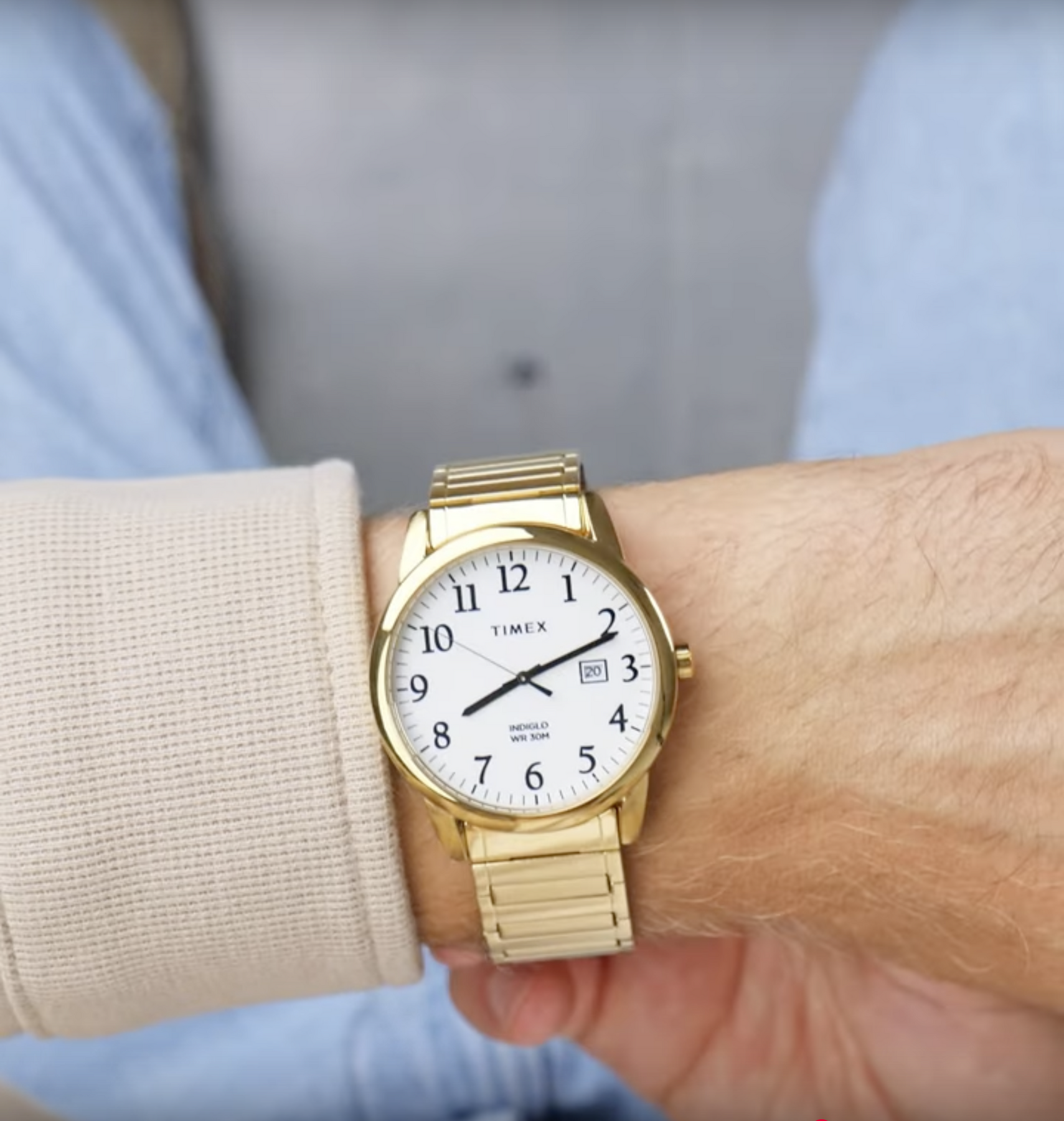 Złoty zegarek na nadgarstku z białą tarczą, czarnymi cyframi arabskimi i napisem \'TIMEX\'. Widoczna jest także data oraz napis \'INDIGLO WR 30M\'.