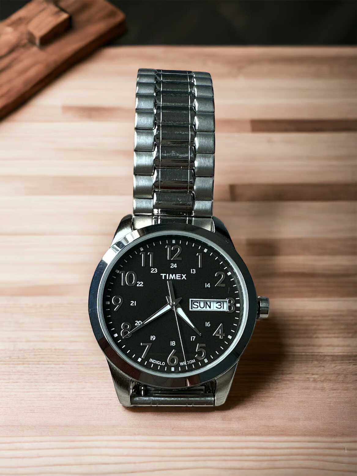 Zegarek męski z metalową bransoletą i czarną tarczą, na której widoczne są srebrne cyfry oraz logo \'TIMEX\'. Na tarczy znajduje się również okienko z datą i dniem tygodnia, wskazujące \'SUN 31\'.