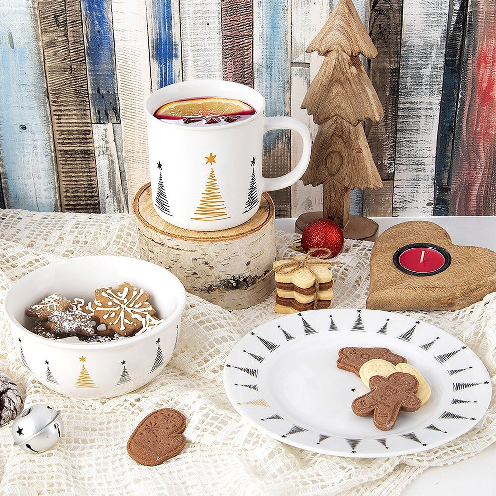 Na obrazie znajduje się zestaw porcelanowych naczyń z motywem choinki, w tym miseczka z piernikami, kubek z napojem oraz talerz z ciasteczkami. W tle widoczne są drewniane ozdoby i kolorowe deski.
