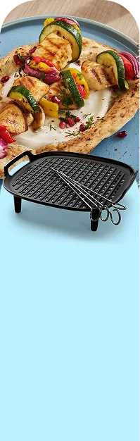 Na niebieskim tle znajduje się czarna kratka grillowa z dwoma metalowymi szpikulcami. W tle widać talerz z grillowanymi warzywami na placku.