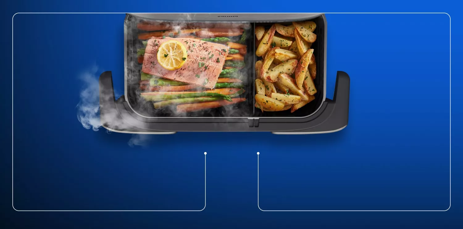 Obraz przedstawia wnętrze frytkownicy beztłuszczowej z dwoma komorami. W jednej komorze znajduje się łosoś z plasterkiem cytryny i warzywami, a w drugiej pieczone ziemniaki; widoczna jest para unosząca się z urządzenia.