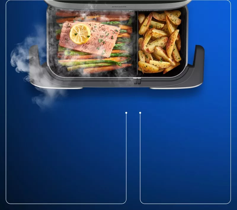 Obraz przedstawia wnętrze frytkownicy z dwoma komorami; w jednej znajduje się łosoś z cytryną i warzywami, a w drugiej pieczone ziemniaki. Widać unoszącą się parę, a na urządzeniu widnieje logo \'Philips\'.