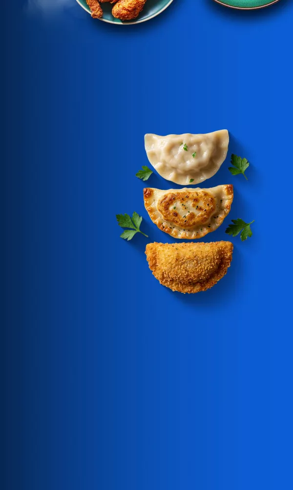 Na niebieskim tle widoczne są trzy pierogi w różnych stanach przygotowania: gotowany, pieczony i smażony. Obok nich leżą gałązki pietruszki.