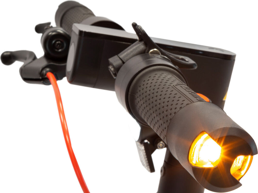 Zbliżenie na kierownicę hulajnogi elektrycznej z widocznym uchwytem i włączonym przednim światłem. W tle widoczny jest czerwony przewód oraz elementy sterujące.