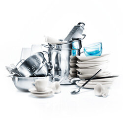 Na obrazie widoczny jest stos naczyń, w tym talerze, filiżanki, miski i sztućce, ułożone w chaotyczny sposób. Naczynia są w większości białe, z wyjątkiem kilku przezroczystych i niebieskich elementów.