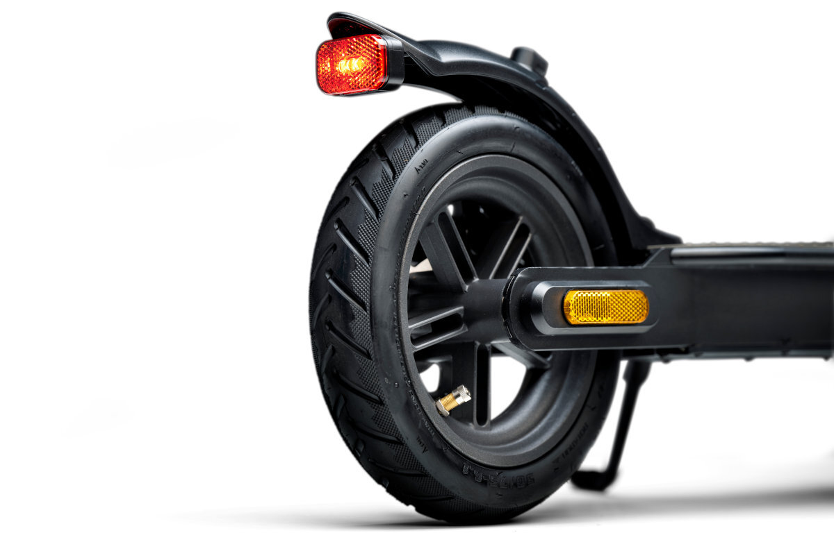 Zbliżenie na tylne koło hulajnogi elektrycznej z czarną oponą i żółtym odblaskiem. Widoczny jest również czerwony odblaskowy element na błotniku.