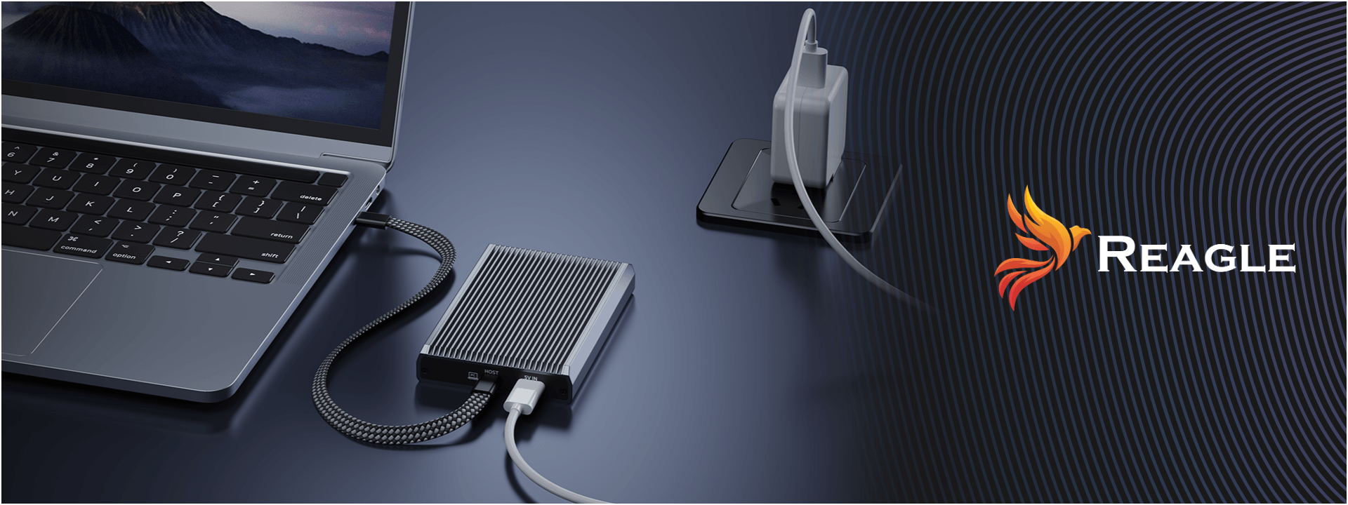 Na obrazie widoczny jest laptop podłączony do dwuzatokowej obudowy na dysk za pomocą kabla USB-C. Obok znajduje się logo Reagle oraz ładowarka podłączona do gniazdka.