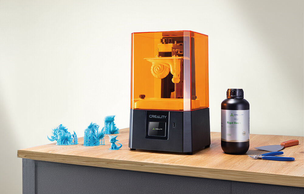 CREALITY Halot R6 drukarka pomarańczowo czarna na blacie obok wydruki