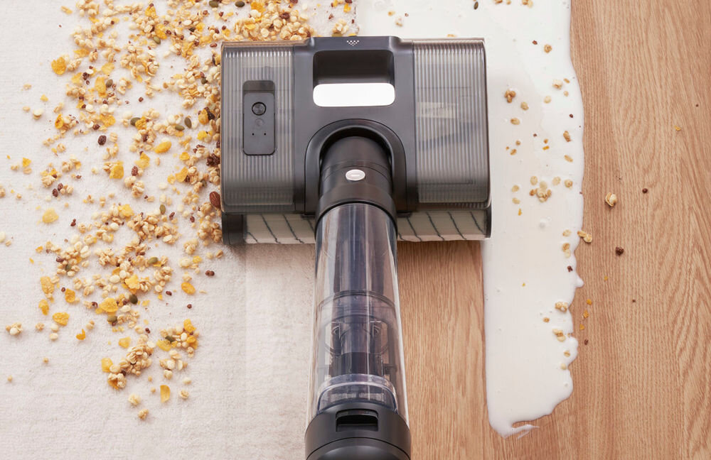 Odkurzacz z aktywnym mopowaniem usuwa rozsypane płatki i rozlany płyn z podłogi. Urządzenie ma przezroczystą rurę i ciemną obudowę.