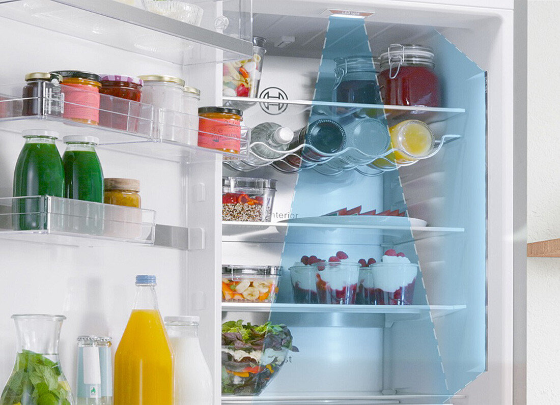 LODÓWKA BOSCH KGN39LBCF BLACK Zdjęcie przedstawia wnętrze lodówki z półkami wypełnionymi produktami, gdzie niebieski trójkątny obszar wizualnie podkreśla strefę równomiernego oświetlenia. Po prawej stronie znajduje się dodatkowe światło LED rozjaśniające przestrzeń chłodziarki Oświetlenie LED jasne światło wnętrze widoczność Energooszczędne