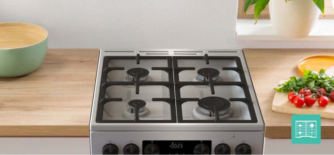 KUCHNIA GORENJE GKS6C71CLI Widok z góry na płytę gazową z palnikami i masywnymi żeliwnymi rusztami, na jednym z palników stoi kremowy garnek, a w tle widać deskę, przyprawy i zioła na blacie