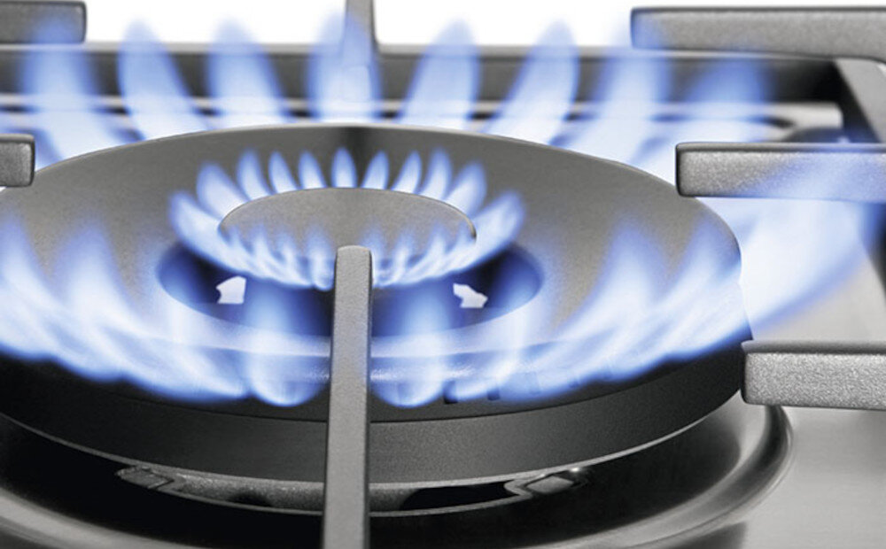 Obraz przedstawia palnik gazowy z niebieskim płomieniem na płycie kuchennej. Widać metalowe ruszty wokół palnika.