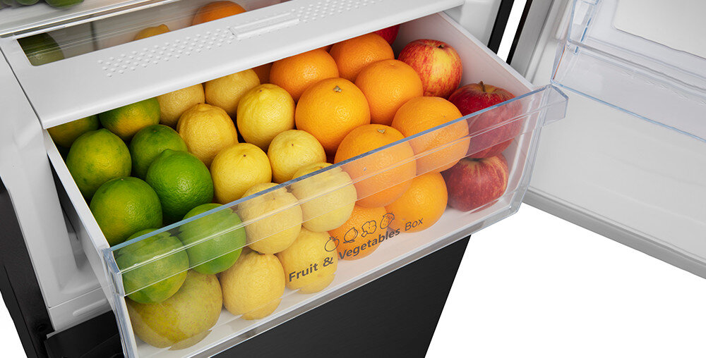 Wnętrze lodówki z otwartą szufladą wypełnioną owocami, takimi jak cytryny, limonki, pomarańcze i jabłka. Na szufladzie widoczny jest napis \'Fruit & Vegetables Box\'.