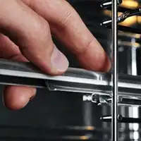 Zbliżenie na rękę trzymającą metalowy uchwyt w piekarniku z widocznymi metalowymi prętami.