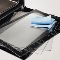 Na obrazie widoczny jest piekarnik z otwartymi drzwiami, na których leży kilka szklanych paneli oraz niebieska ściereczka. Panele mają czarne ramki z oznaczeniami i symbolami.