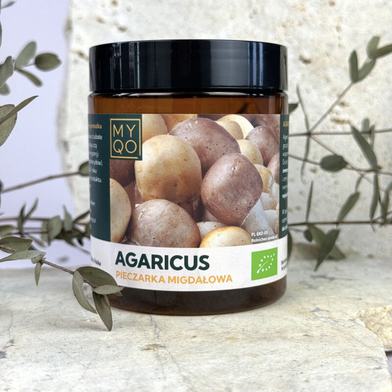 Słoik z etykietą przedstawiającą różne grzyby, z napisem \'MYQO AGARICUS PIECZARKA MIGDAŁOWA\'. W tle widoczne są gałązki z liśćmi.