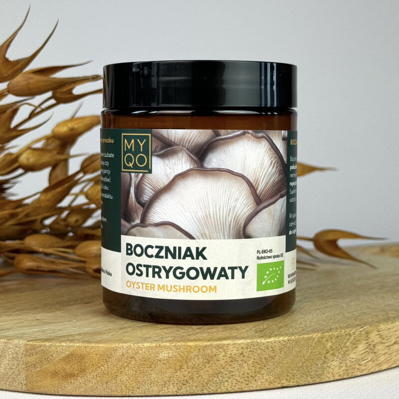 Słoik z etykietą przedstawiającą boczniaki, z napisem \'BOCZNIAK OSTRYGOWATY OYSTER MUSHROOM\'. Obok słoika znajdują się suche gałązki na drewnianej podstawce.