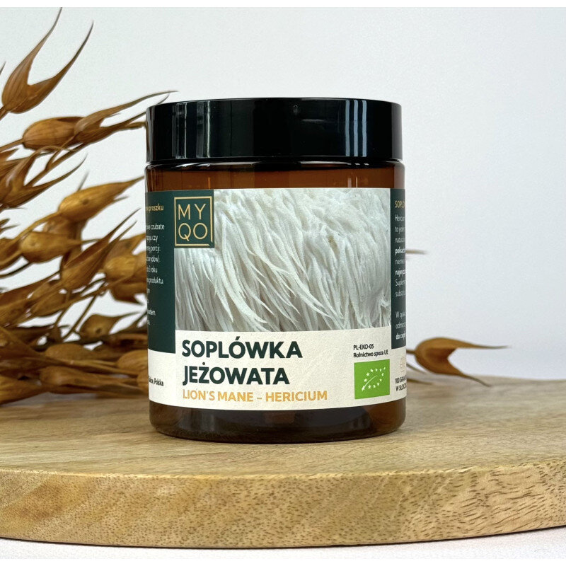 Słoik z ciemnego szkła z czarną zakrętką, na etykiecie napis \'Soplówka Jeżowata Lion\'s Mane - Hericium\'. W tle widoczne są suche gałązki roślin.