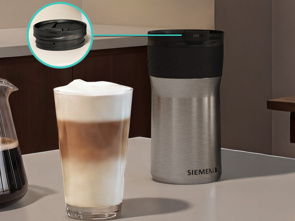 Na blacie stoi stalowy termos z czarną pokrywką, obok szklanka z kawą latte. Na termosie widoczne jest logo \'SIEMENS\'.