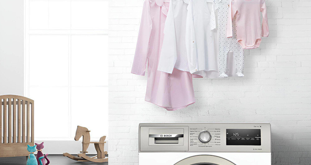 Pralka z widocznym panelem sterowania i logo BOSCH, na której suszą się różowe i białe ubrania. W tle znajduje się jasna ściana i drewniany konik na biegunach.
