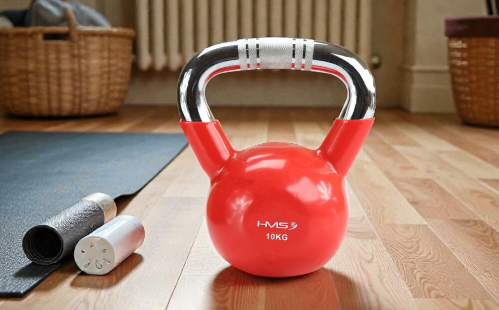 Kettlebell HMS KTC10 (10 kg) pokój drewniana podłoga kettlebell stoi na podłodze obok mata do ćwiczeń w tle kosz kwiat kaloryfer chromowany, stalowy uchwyt z precyzyjnym radełkowaniem pewny i stabilny chwyt teksturowana powierzchnia ogranicza ślizganie się dłoni zwiększa kontrolę nad ciężarem chromowana powłoka odpowiada za odporność na korozję i ścieranie