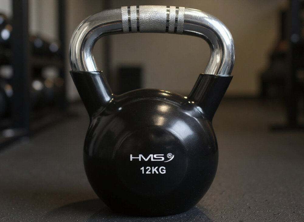 Kettlebell HMS KTC12 (12 kg) siłownia kettlebell stoi na podłodze w tle przyrządy do ćwiczeń trening siłowy trening kondycyjny zdrowie wszechstronne zastosowanie