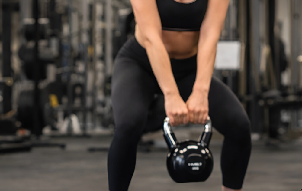 Kettlebell HMS KTC12 (12 kg) sala gimnastyczna osoba w stroju sportowym trzyma kettlebell w dłoniach wykonuje ćwiczenia chromowany, stalowy uchwyt z precyzyjnym radełkowaniem pewny i stabilny chwyt teksturowana powierzchnia ogranicza ślizganie się dłoni zwiększa kontrolę nad ciężarem chromowana powłoka odpowiada za odporność na korozję i ścieranie