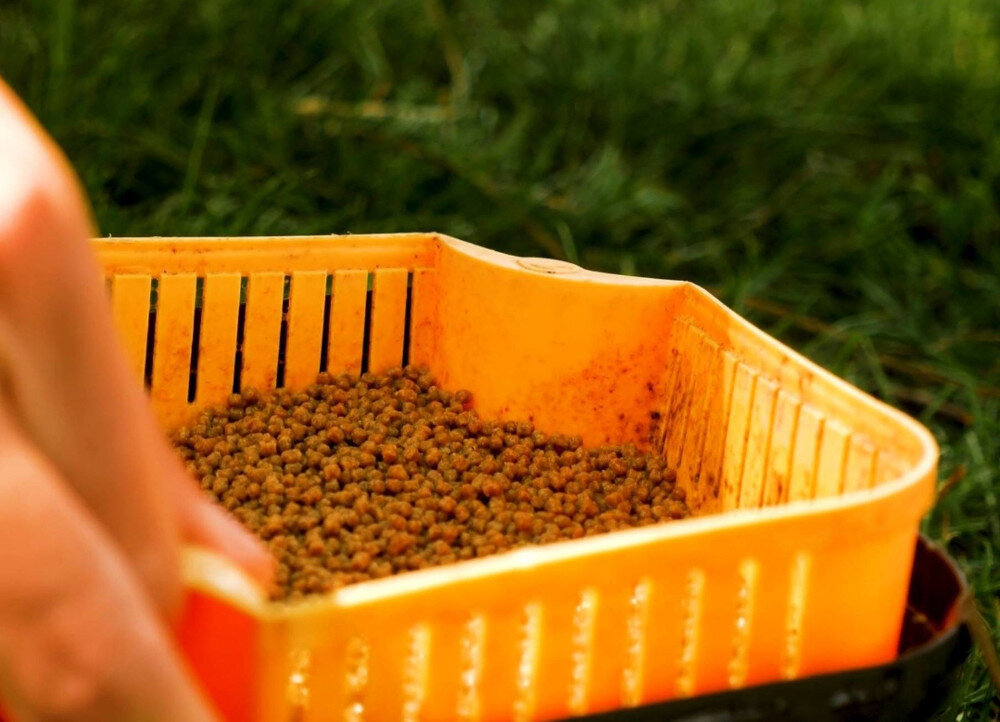 Pellet BAITNOW OOriginal Coarse 2 mm (800 g) koszyk z pelletem gotowy do namoczenia trzymany w dłoni na tle trawy