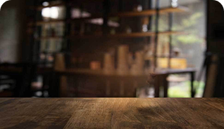 Drewniany stół na tle rozmytego wnętrza kawiarni z półkami i roślinnością.