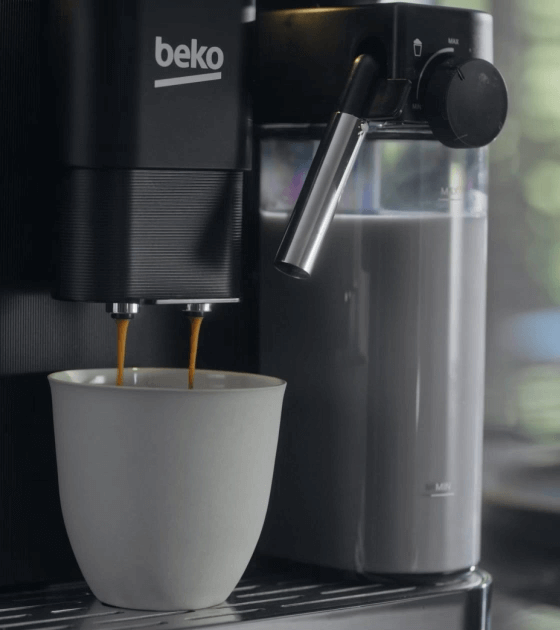 Ekspres do kawy z logo \'beko\' nalewa kawę do białej filiżanki. Obok znajduje się pojemnik z mlekiem i dysza do spieniania.