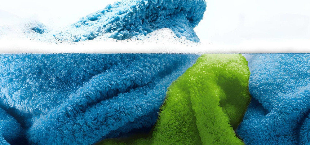 Na obrazie widoczne są niebieskie i zielone ręczniki zanurzone w wodzie z pianą na powierzchni.