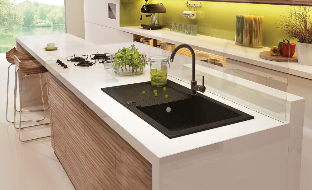 Nowoczesna kuchnia z wyspą, na której znajduje się czarny zlewozmywak jednokomorowy z ociekaczem. W tle widoczne są zielone akcenty dekoracyjne oraz sprzęty kuchenne.