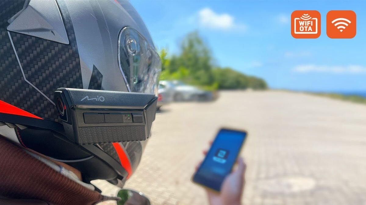 MIO MiVue MP20 zarządzaj kamerą bezpośrednio ze swojego smartfona zintegrowanemu modułowi Wi-Fi dedykowanej aplikacji MiVue™ Pro przesyłania filmów i tworzenia kopii zapasowych w czasie rzeczywistym Moduł Wi-Fi aktualizacje oprogramowania układowego (technologia OTA: Over The Air) - Wideorejestrator zamontowany na kasku motocyklowym w trakcie postoju na poboczu, z widocznym smartfonem w dłoni oraz ikonami łączności bezprzewodowej.