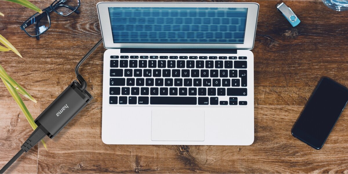 Widok z góry na czarną ładowarkę Hama USB-C (zasilacz) podłączoną do laptopa na drewnianym biurku.